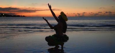 A dancer performing a traditional Chamorro dance at sunset on a Guam beach